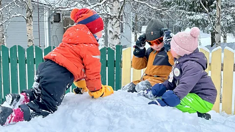 Children dressed in hats and warm outdoor clothing kneel on a mound of snow (Credit: Erika Benke)