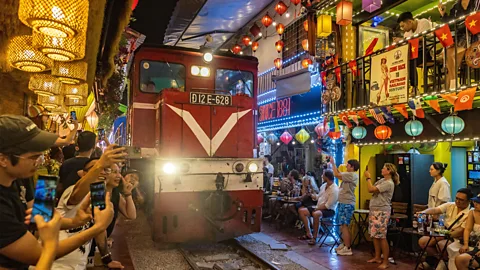 Tourists take photos as a train rushes through Hanoi's Train Street (Credit: Alamy)