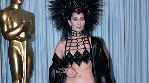 Cher in a revealing black top and jacket and black headress at the 1986 Oscars (Credit: Getty Images)