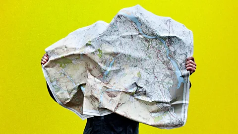 A person trying to read a crumpled map as the wind blows it against their face (Credit: BBC/ Getty Images)