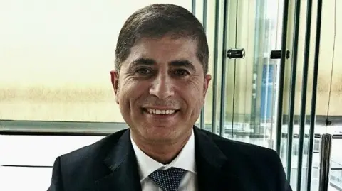 Head and shoulders shot of Jihad Quzmar, wearing a tie and jacket and smiling towards the the camera