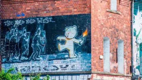 The famous Banksy art work 'The Mild Mild West' at Stokes Croft. It shows a large mural on the side of a red-brick building, depicting a bear throwing a Molotov cocktail at a group of police officers behind plastic shields.