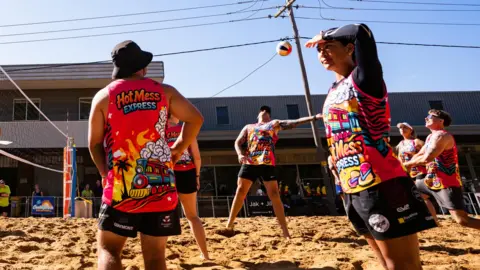 A woman shields her face with her hand as she looks at an inland beach volleyball court