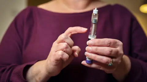 A woman in a burgandy top holds a weight loss injection pen