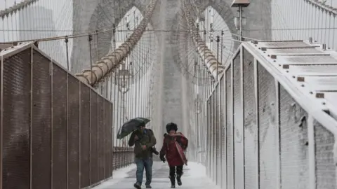 People walk across the Brooklyn Bridge as snow falls during a winter storm in New York Cit on 22 February 2026.