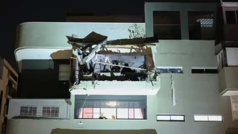 Rescuers work through rubble at an apartment hit by a bomb. It is night time and they wear head torches. 