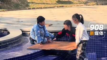 三位小朋友在干涸的泳池里，坐在木板上模仿滑雪