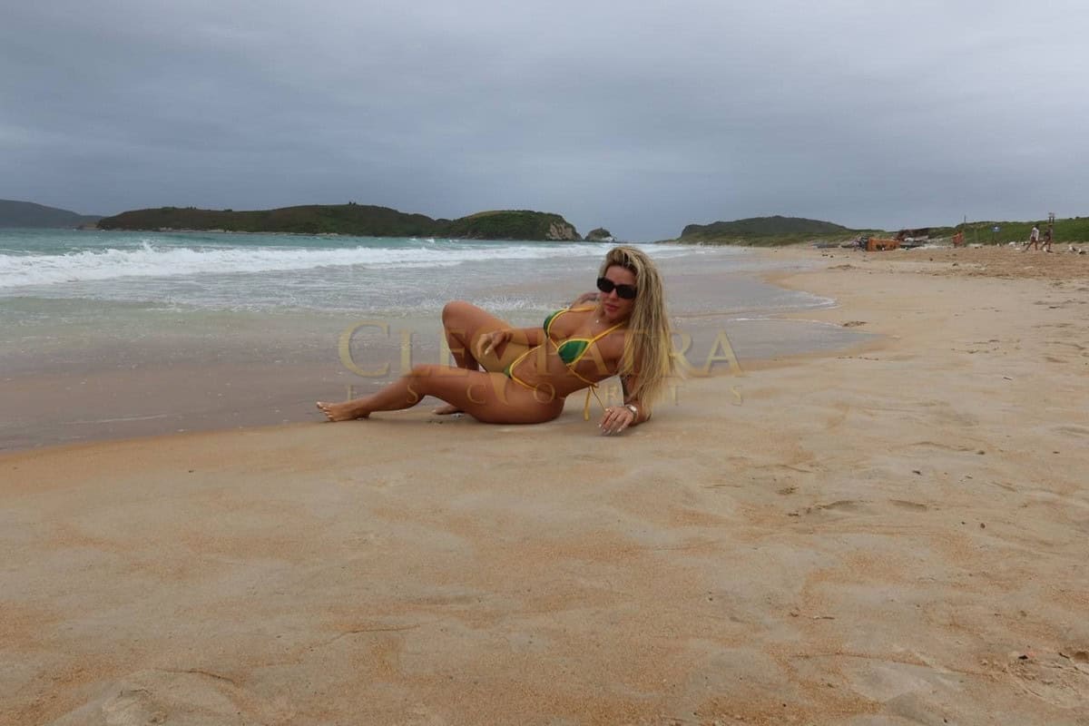 Seductive escort woman relaxing on a sandy beach in London, stunning bikini, luxury service.