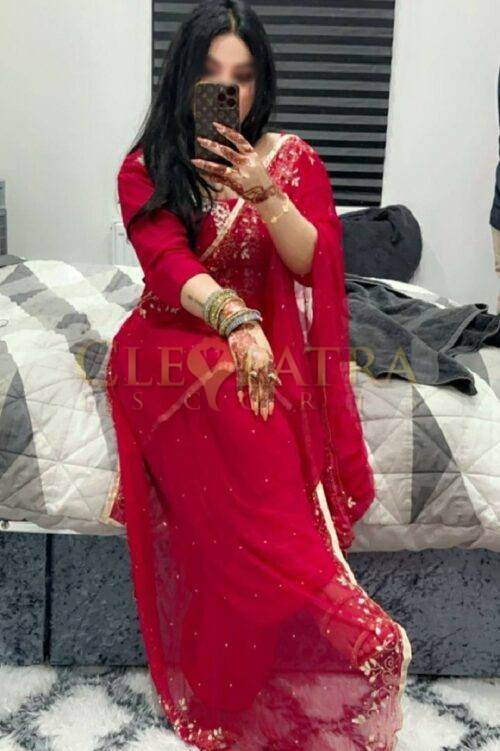 Luxurious Indian woman in red traditional saree taking mirror selfie in bedroom.