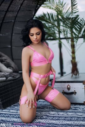 Petite girl with black hair in a sexy pink bikini kneeling on a bed